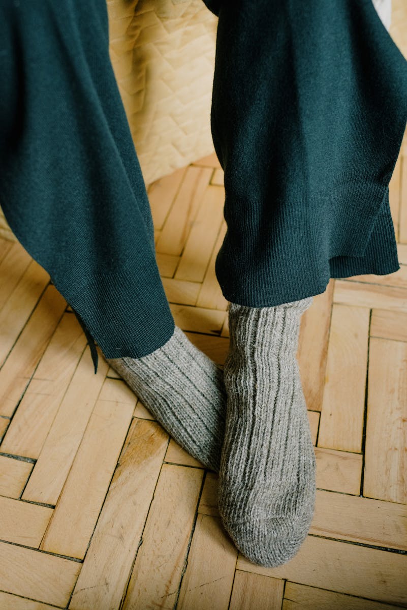 Woolen knitted socks over black pants on a wooden parquet floor.